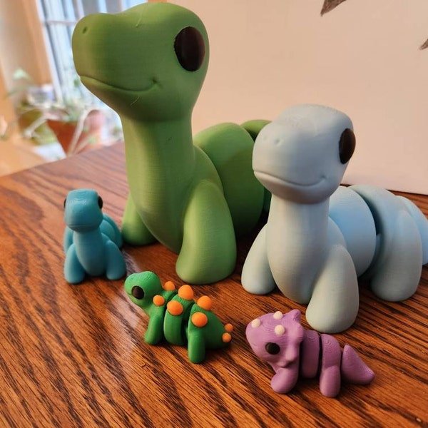 Cinco dinossauros articulados impressos em 3D nas cores verde, azul, roxo e laranja