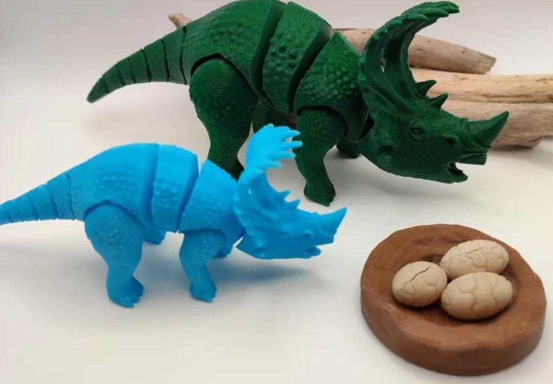 Triceratops azul e Sinoceratops verde impressos em 3D ao lado de um ninho com ovos