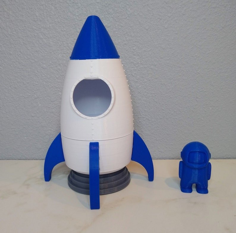 Foguete branco e azul com astronauta, ambos impressos em 3D